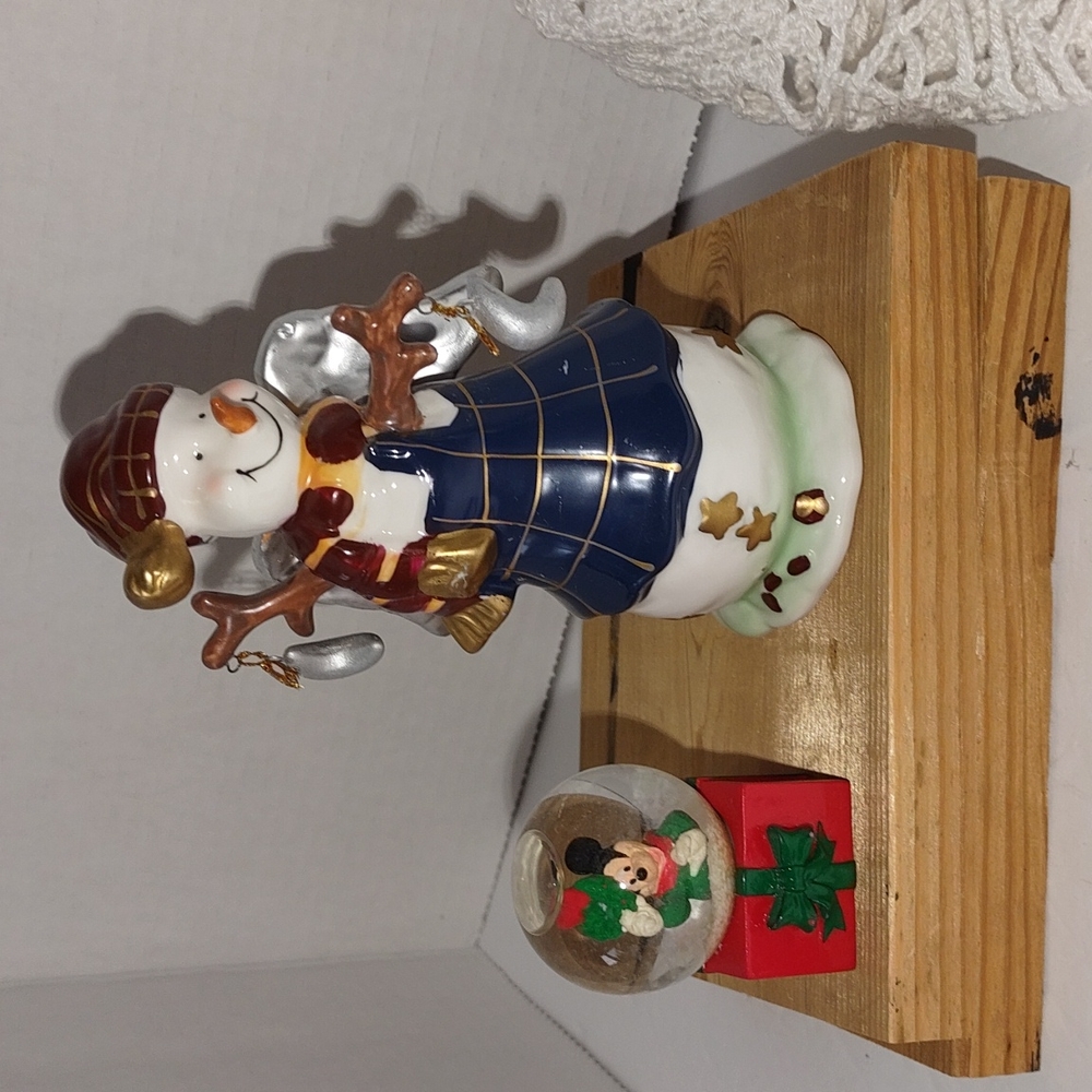 A Snowman holding Little Moons and Mickey Mouse miniature in a snow globe
